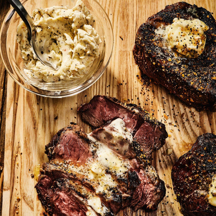 A close-up of a delicious steak with butter and herbs on a wooden cutting board.