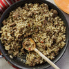A skillet filled with a mixture of rice and ground meat is being stirred with a wooden spoon.