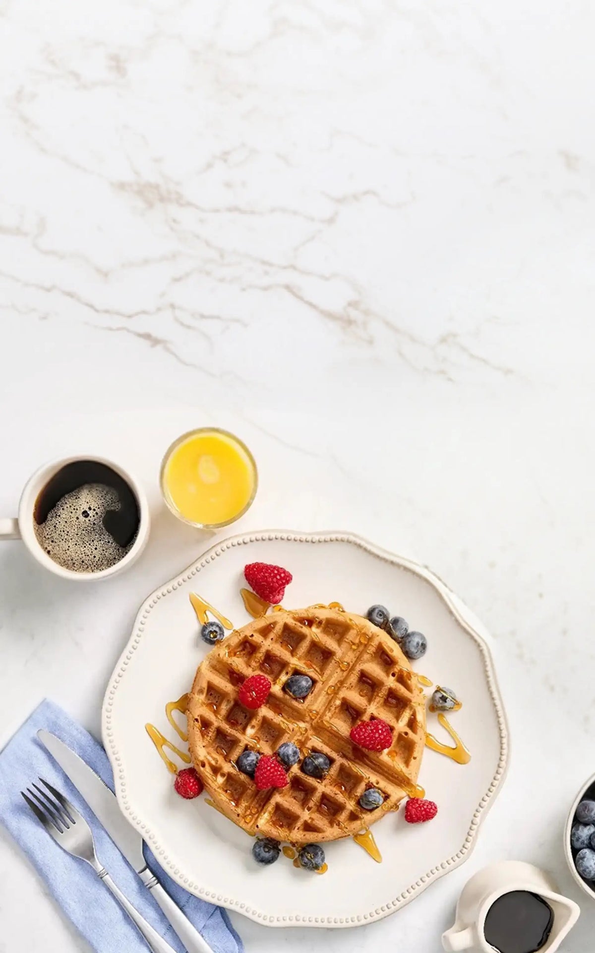 Waffle with berries on a plate with coffee and syrup on a marble surface