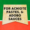 A vintage-style sign with the text FOR ACHIOTE PASTES, &amp; ADOBO SAUCES on a yellow background.