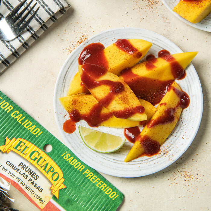 A plate of mango slices with chili powder and a lime wedge, with a El Guapo brand label in the foreground.
