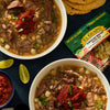 Two bowls of El Guapo soup with meat, beans, and a red sauce on top.