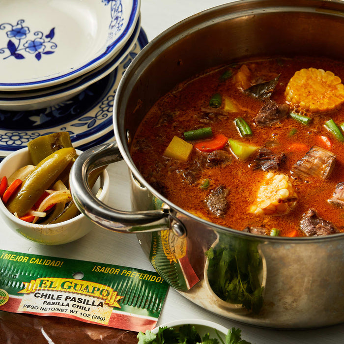 A pot of El Guapo Chile Pasilla Pasilla Chili with a bowl of pickled peppers and onions.