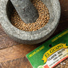 A mortar and pestle filled with coriander seeds, next to a package of El Guapo Cilantro Bolita.