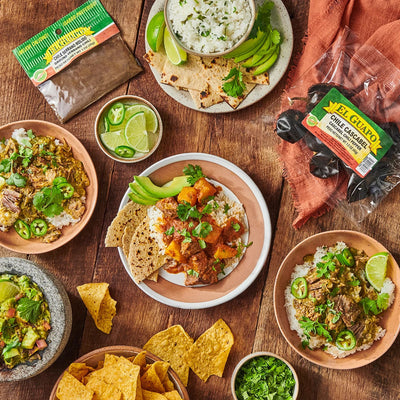 overhead shot of el guapo peppers, chili, and various latin dishes covered with avocados, jalapenos, lime, cilantro and tortilla chips