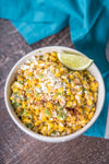 A bowl of Mexican street corn with cotija cheese, chili powder, and lime.