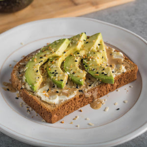 A slice of toast topped with avocado, cream cheese, and sesame seeds.