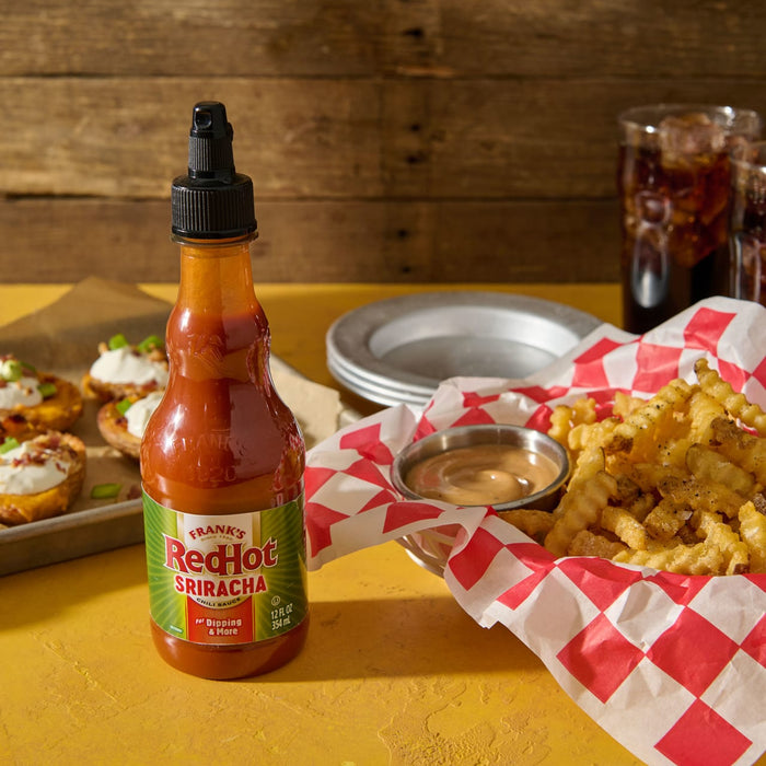 A bottle of Franks RedHot Sriracha chili sauce next to a plate of loaded potato skins and a bowl of curly fries with dipping sauce.