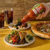 A hand pours Franks RedHot Sriracha Chili Sauce onto a pita bread filled with chicken, vegetables, and cilantro.