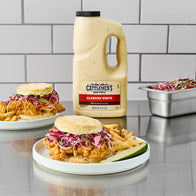 Cattlemen's Alabama White sauce bottle with plates of food on a reflective surface.
