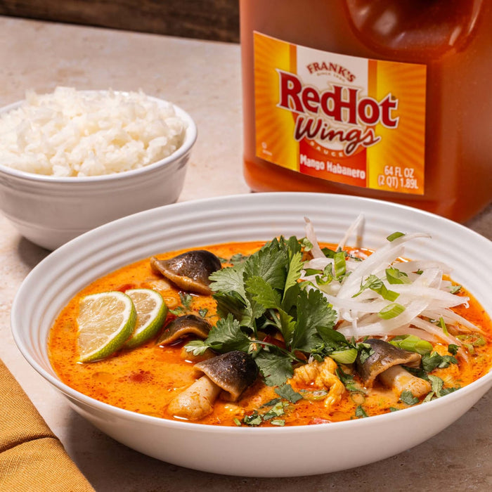 A bowl of Tom Kha Gai soup with a bottle of Franks RedHot Mango Habanero sauce in the background.