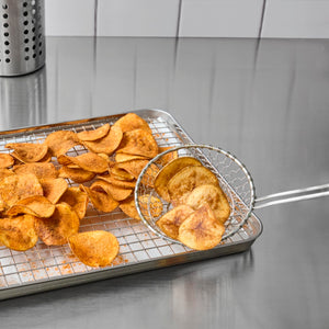 A metal tray with a wire rack holds a pile of homemade potato chips, some of which are being scooped up with a wire skimmer.