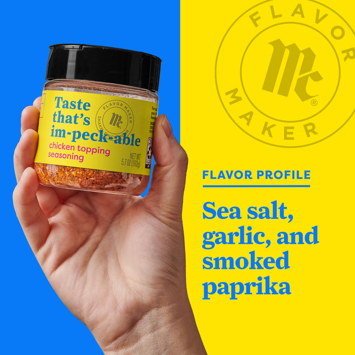 A hand holds a jar of Flavor Makers im-peck-able chicken topping seasoning, with a yellow background showing the Flavor Maker logo and the flavor profile.