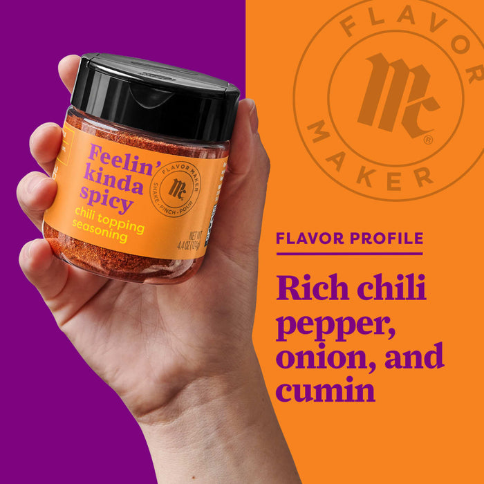 A hand holds a jar of Flavor Maker Feelin Kinda Spicy chili topping seasoning, with the Flavor Maker logo and flavor profile in the background.