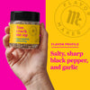 A hand holds a jar of Flavor Makers You Crack Me Up egg topping seasoning, with a yellow background showing the Flavor Maker logo and the flavor profile.