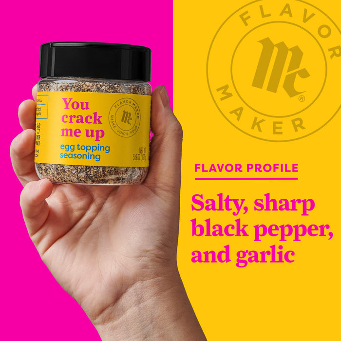 A hand holds a jar of Flavor Makers You Crack Me Up egg topping seasoning, with a yellow background showing the Flavor Maker logo and the flavor profile.