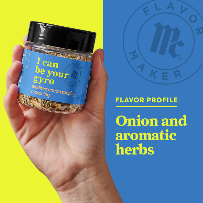 A hand holds a jar of Flavor Makers I Can Be Your Gyro seasoning, a Mediterranean topping blend with onion and aromatic herbs.