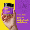 A hand holds a jar of Flavor Maker Pasta-tively Obsessed pasta topping seasoning, with a purple background that says Flavor Profile: Savory garlic, basil, and cheese.