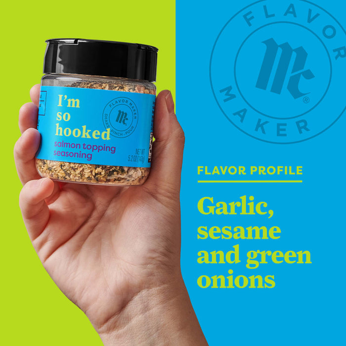 A hand holds a jar of Flavor Makers Im So Hooked salmon topping seasoning, with a blue background that says Flavor Maker and the flavor profile of garlic, sesame, and green onions.