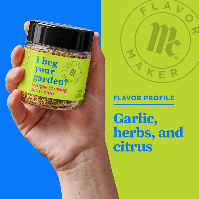 A hand holds a Flavor Maker spice jar labeled I beg your garden? with a veggie topping seasoning.