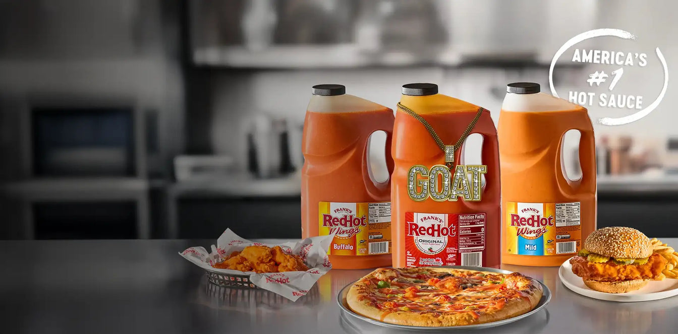 Three bottles of RedHot sauce with a pizza, burger, and fries on a table.