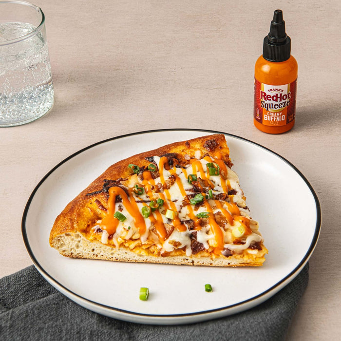 A slice of pizza topped with Frank's RedHot Squeeze Creamy Buffalo Sauce.