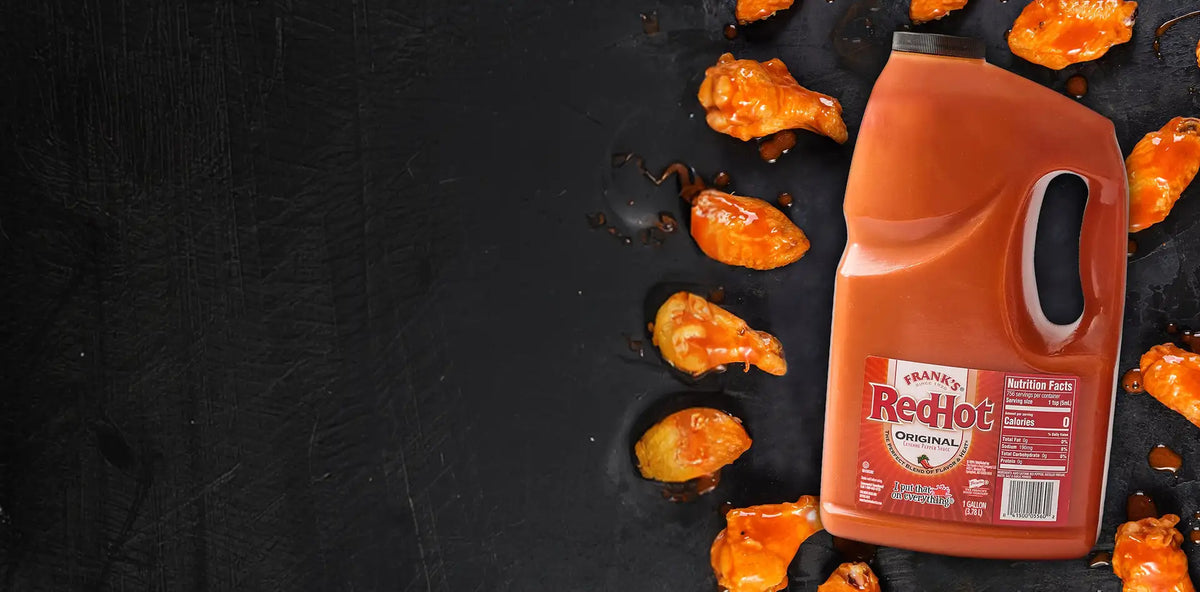 Bottle of Frank's RedHot sauce with hot wings on a black background