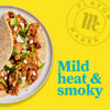 A plate of chicken tacos with avocado, feta cheese, and lettuce with the Flavor Maker logo and the text Mild heat &amp; smoky in the background.