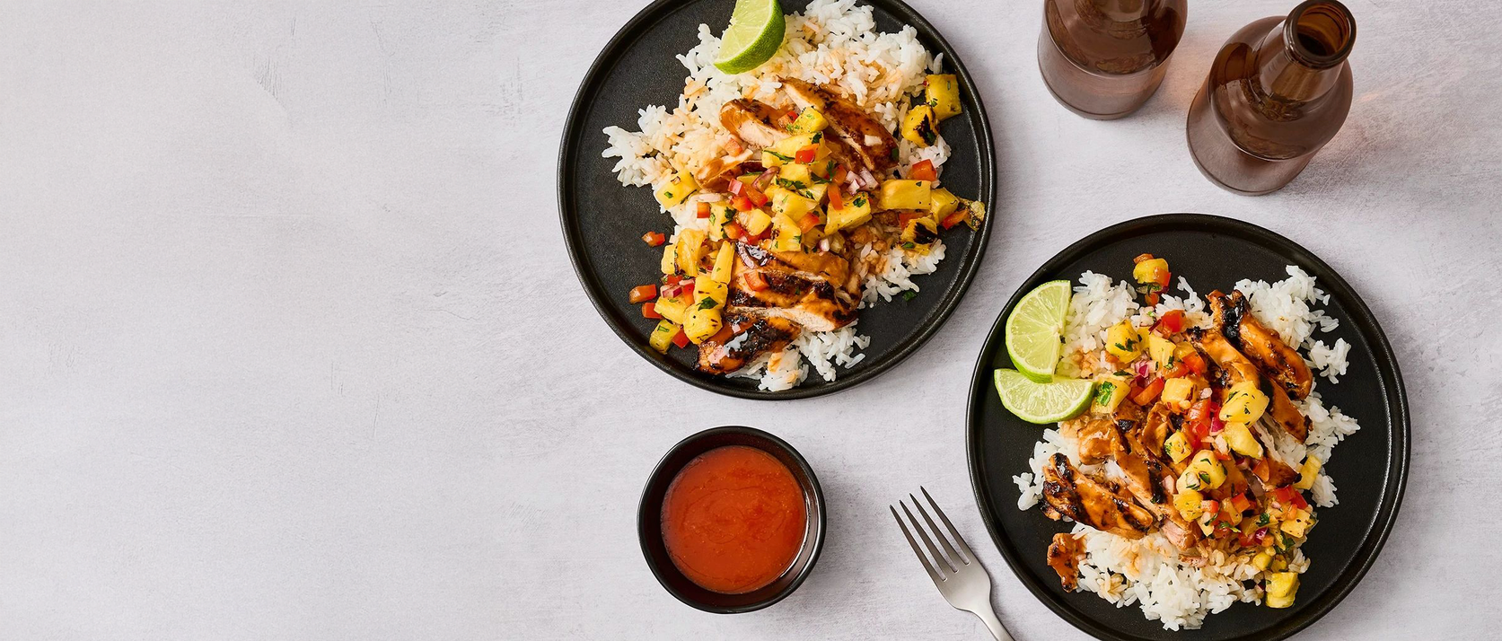 Two plates of food with rice, chicken, and vegetables on a light gray background.