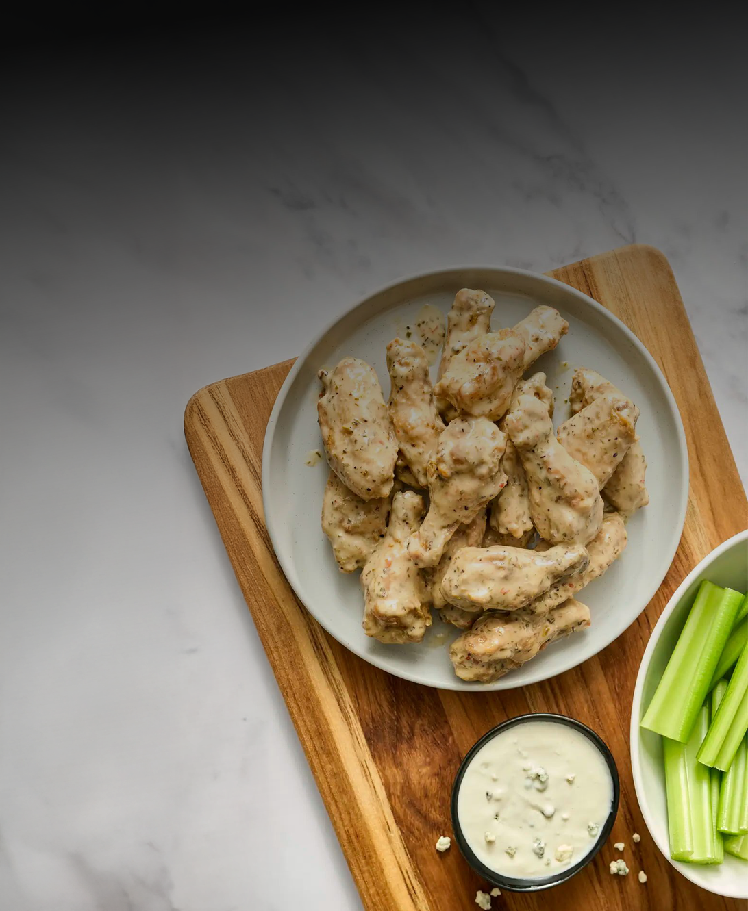 Plated chicken wings with a side of celery and sauce on a wooden board.
