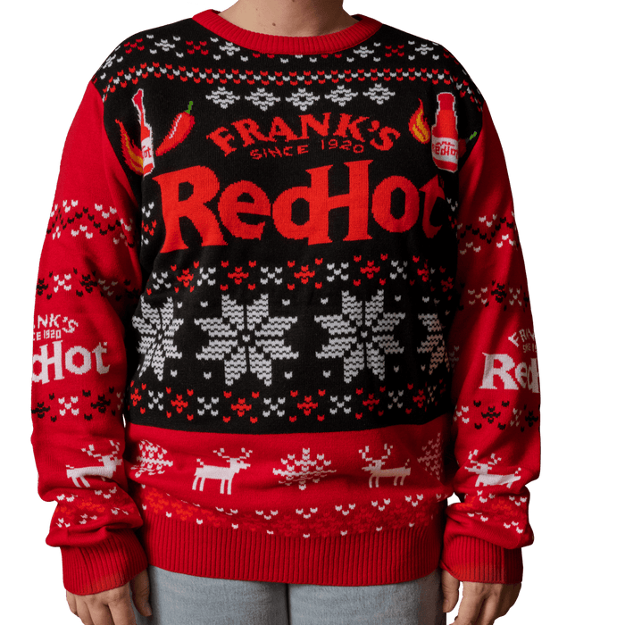 A person wears a festive holiday sweater featuring the Frank s RedHot logo along with illustrations of hot sauce bottles and chili peppers.