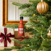 A miniature bottle of Frank s RedHot Original Cayenne Pepper Sauce hangs as a festive ornament on a decorated Christmas tree next to wrapped gifts.