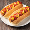 Two hot dogs in buns are generously topped with French'S Tomato Ketchup (Case Of 9) and yellow mustard, presented on a white plate against a dark wooden background.