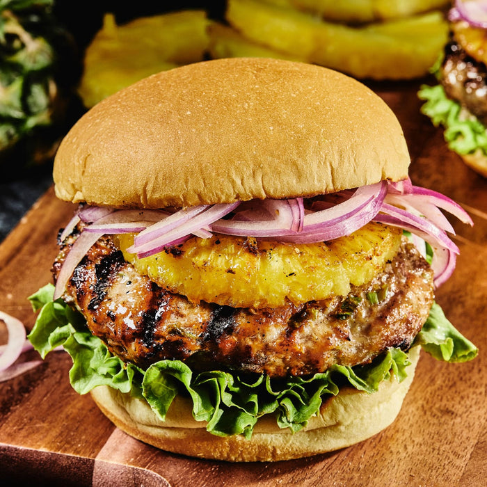 A close-up of a grilled pineapple and red onion burger on a wooden cutting board.