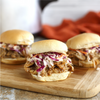 Three pulled pork sliders with coleslaw on a wooden cutting board.