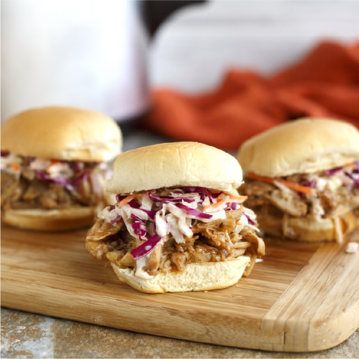 Three pulled pork sliders with coleslaw on a wooden cutting board.