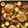 A close-up of a baking sheet with roasted chicken, potatoes, carrots, and onions.
