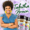 Tabitha Brown, a woman with an afro, smiles while holding two McCormick Very Good Garlic seasoning jars.