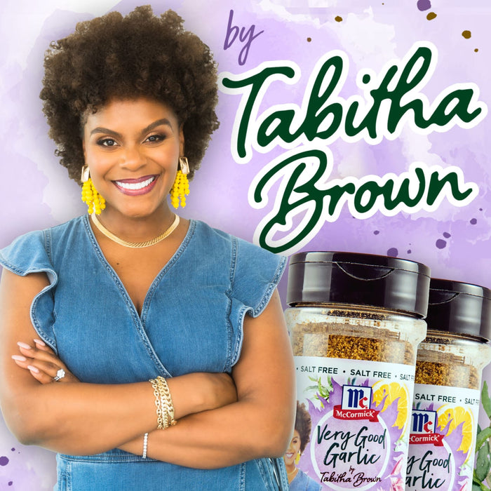 Tabitha Brown, a woman with an afro, smiles while holding two McCormick Very Good Garlic seasoning jars.