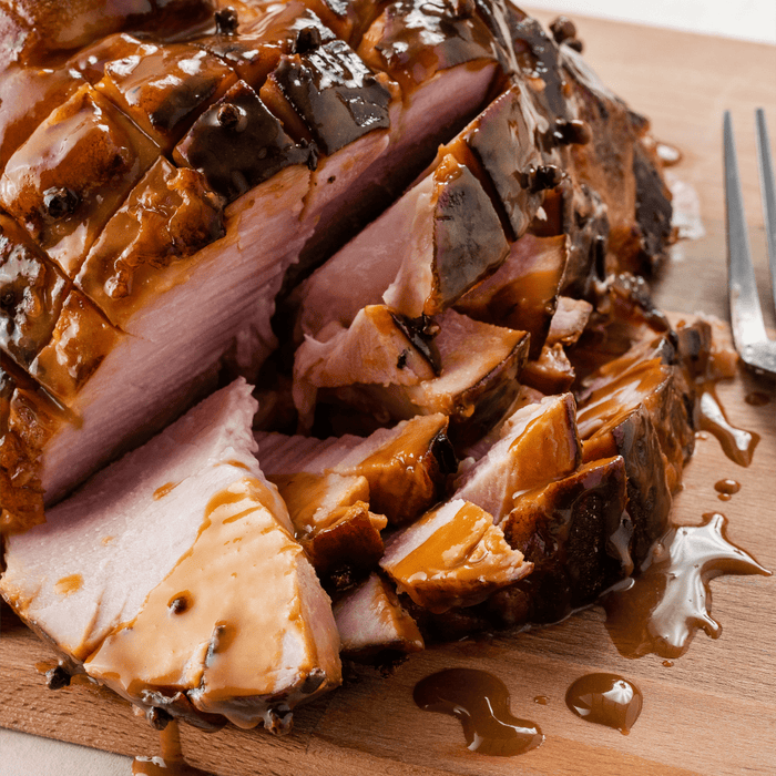 A close-up of a sliced ham with a brown glaze on a wooden cutting board.