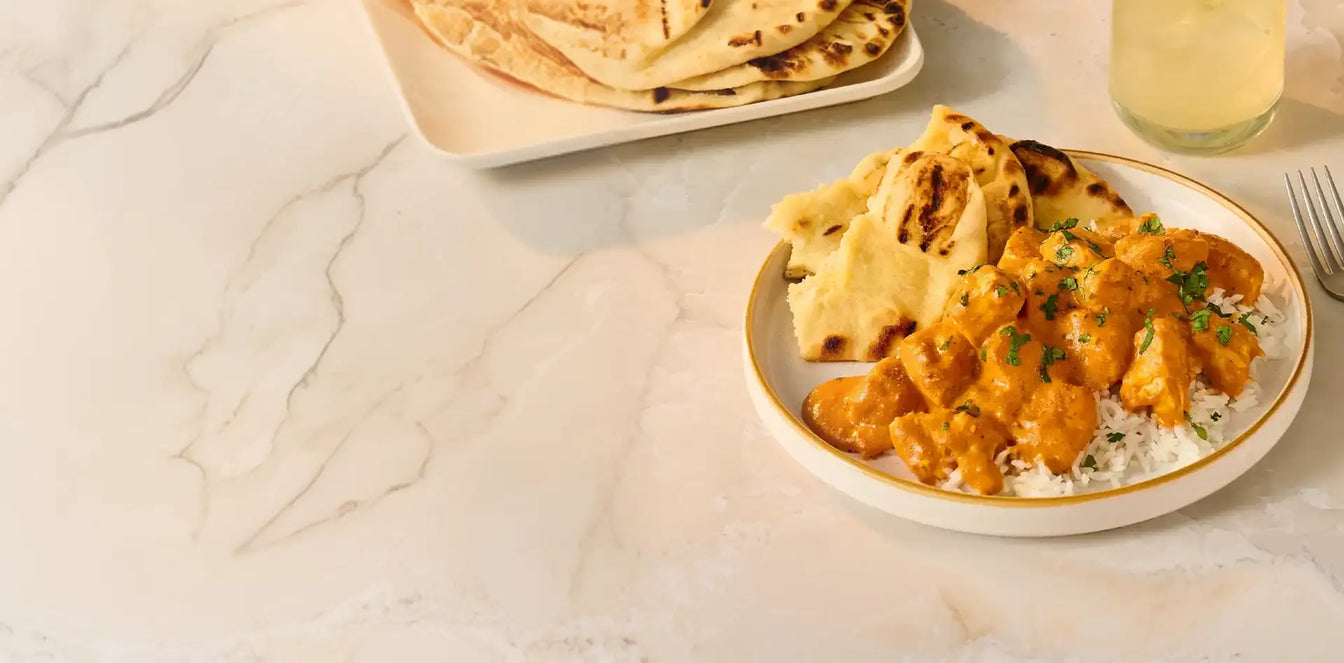 Plated dish of curry with naan bread on a marble surface