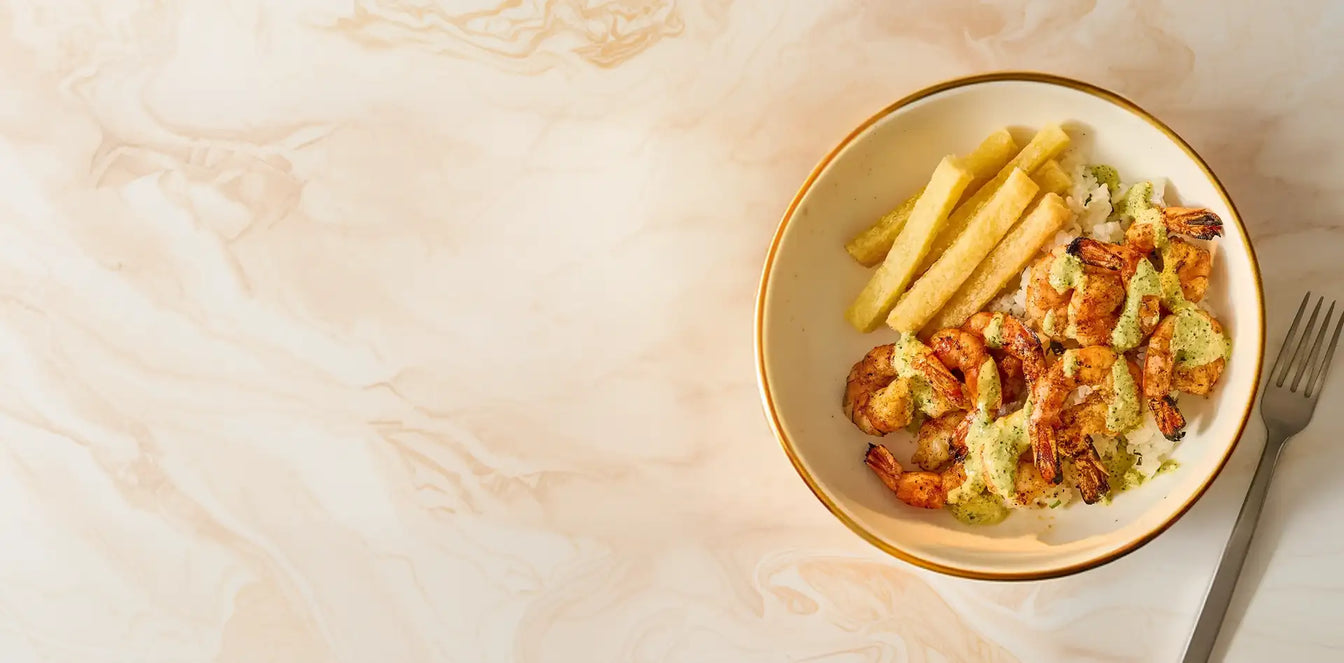 Bowl of pasta with shrimp and avocado sauce on a light wooden surface
