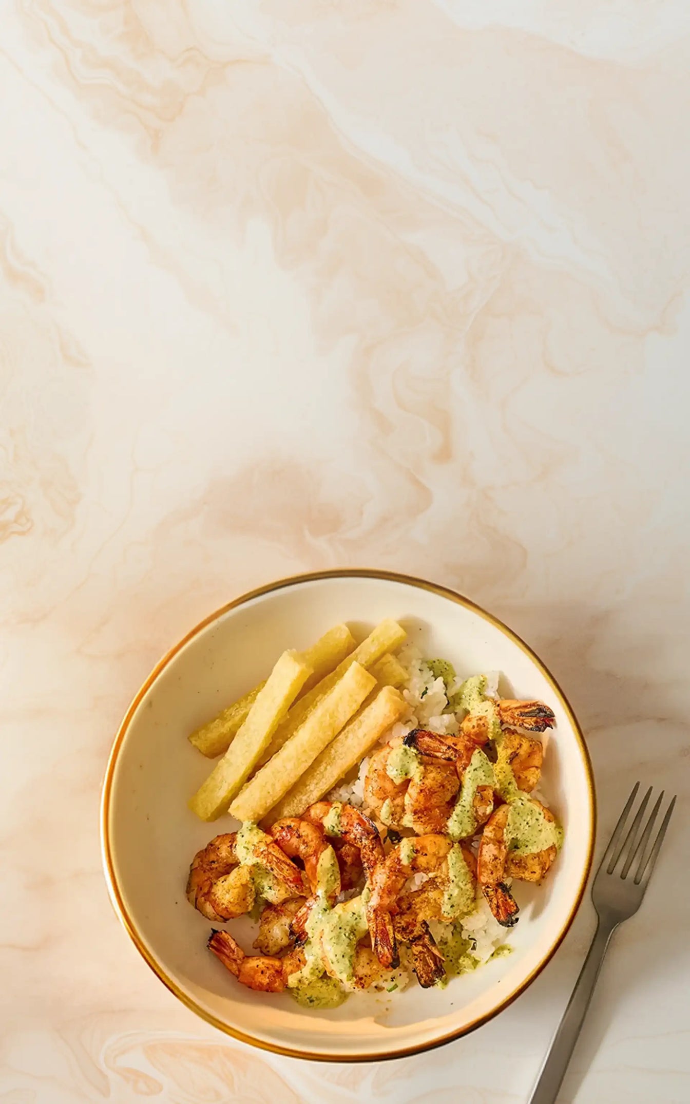 Dish with shrimp, fries, and a sauce on a marble surface