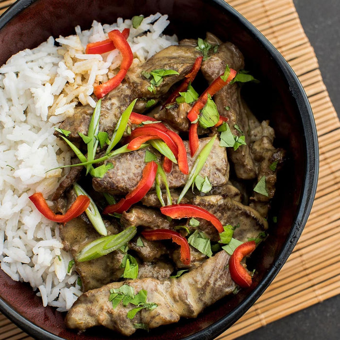 A bowl of rice topped with a creamy beef and vegetable stir fry.