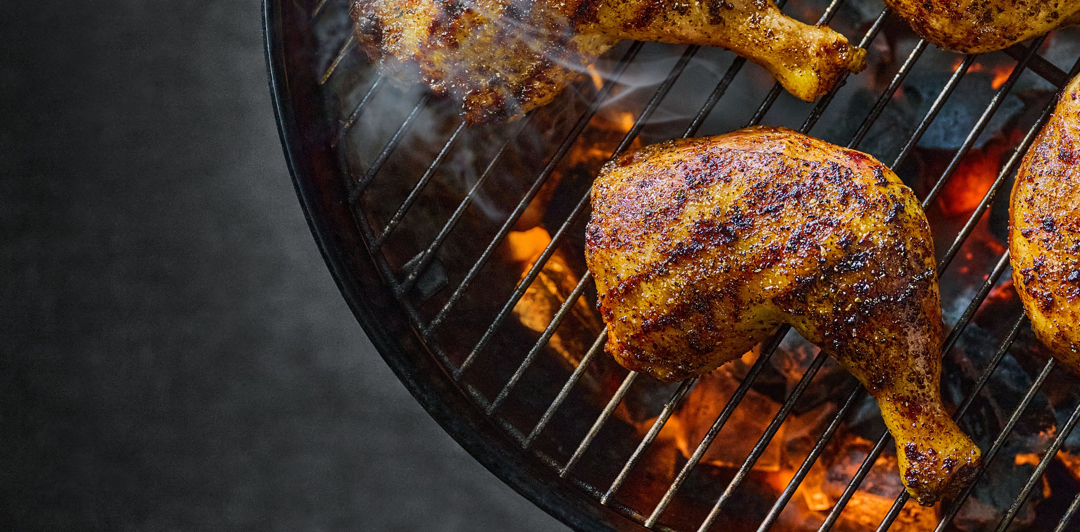 Grilled chicken legs on a barbecue grill with flames and smoke.
