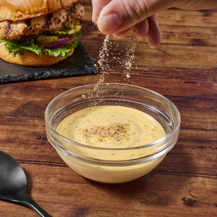 A hand sprinkles seasoning over a bowl of yellow sauce.