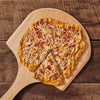 A pizza with bacon, cheese, and red onion on a wooden cutting board.