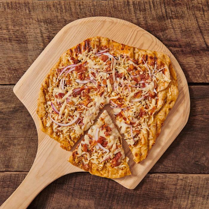 A pizza with bacon, cheese, and red onion on a wooden cutting board.