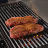 Two seasoned steaks are on a hot grill.