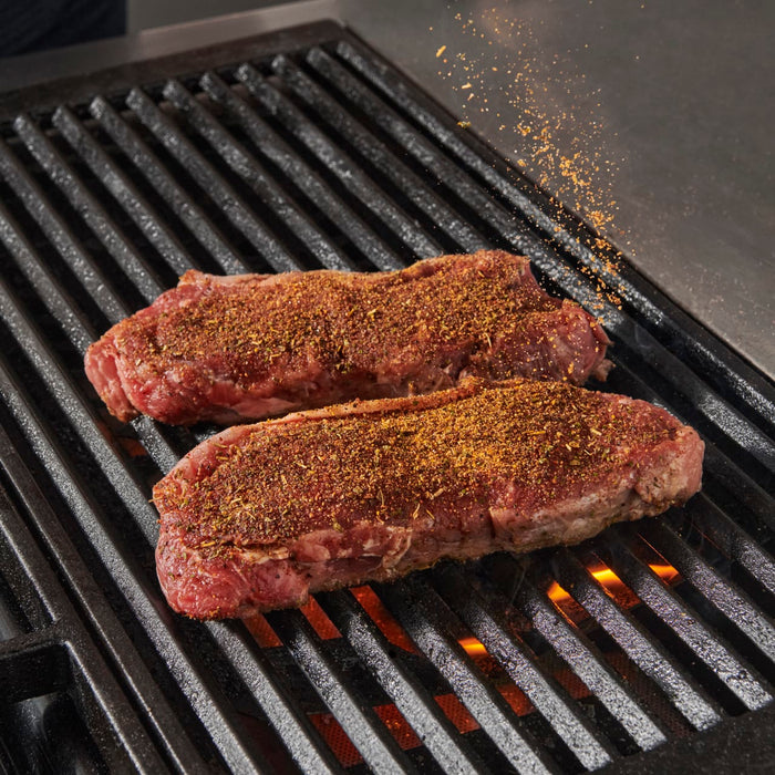 Two seasoned steaks are on a hot grill.